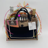 Gift presented in a jute & black cotton handbag, premium snacks, beverages and decorative ribbons on a light gray background